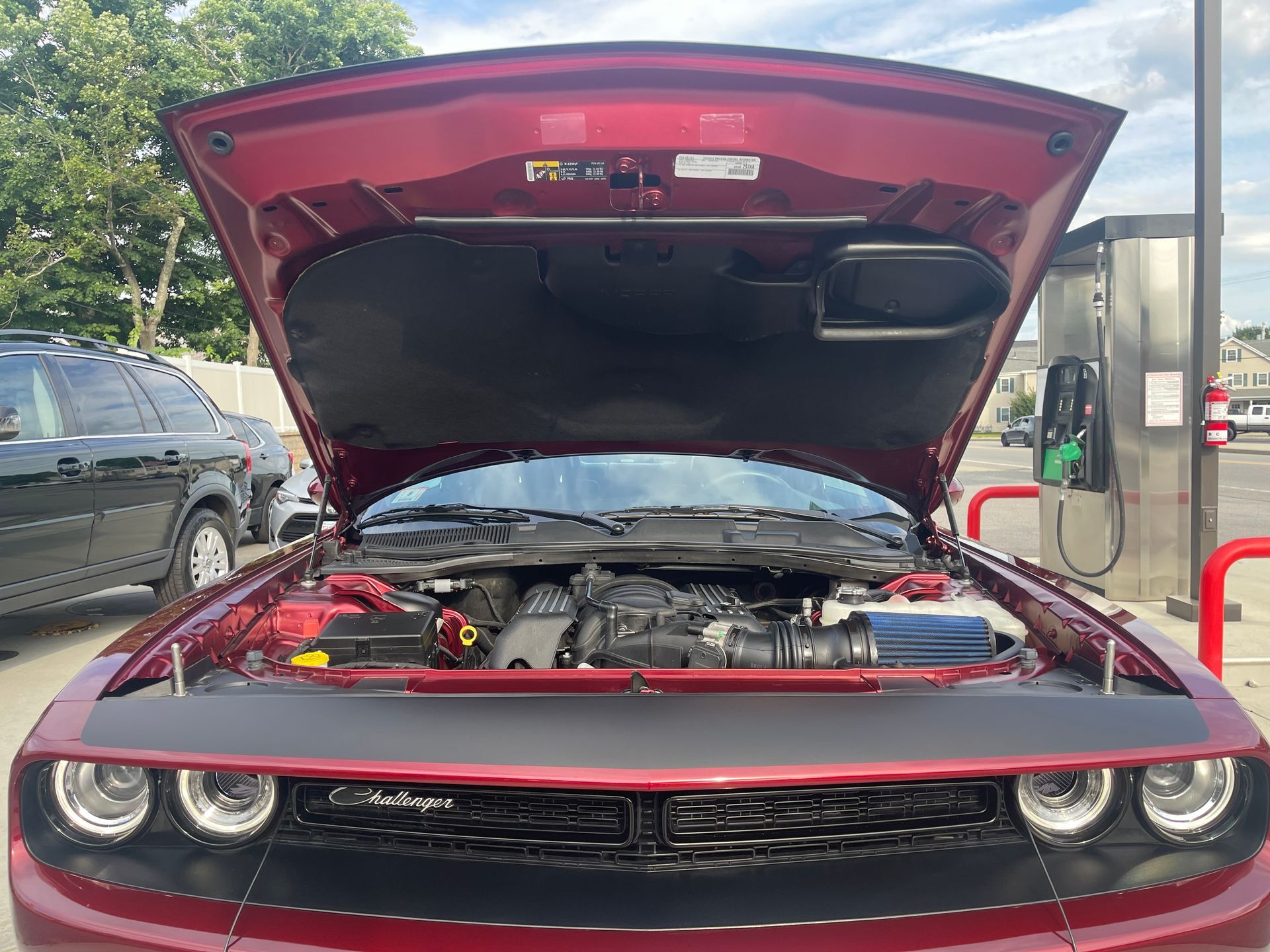 The hood of a red dodge challenger is open at a gas station.