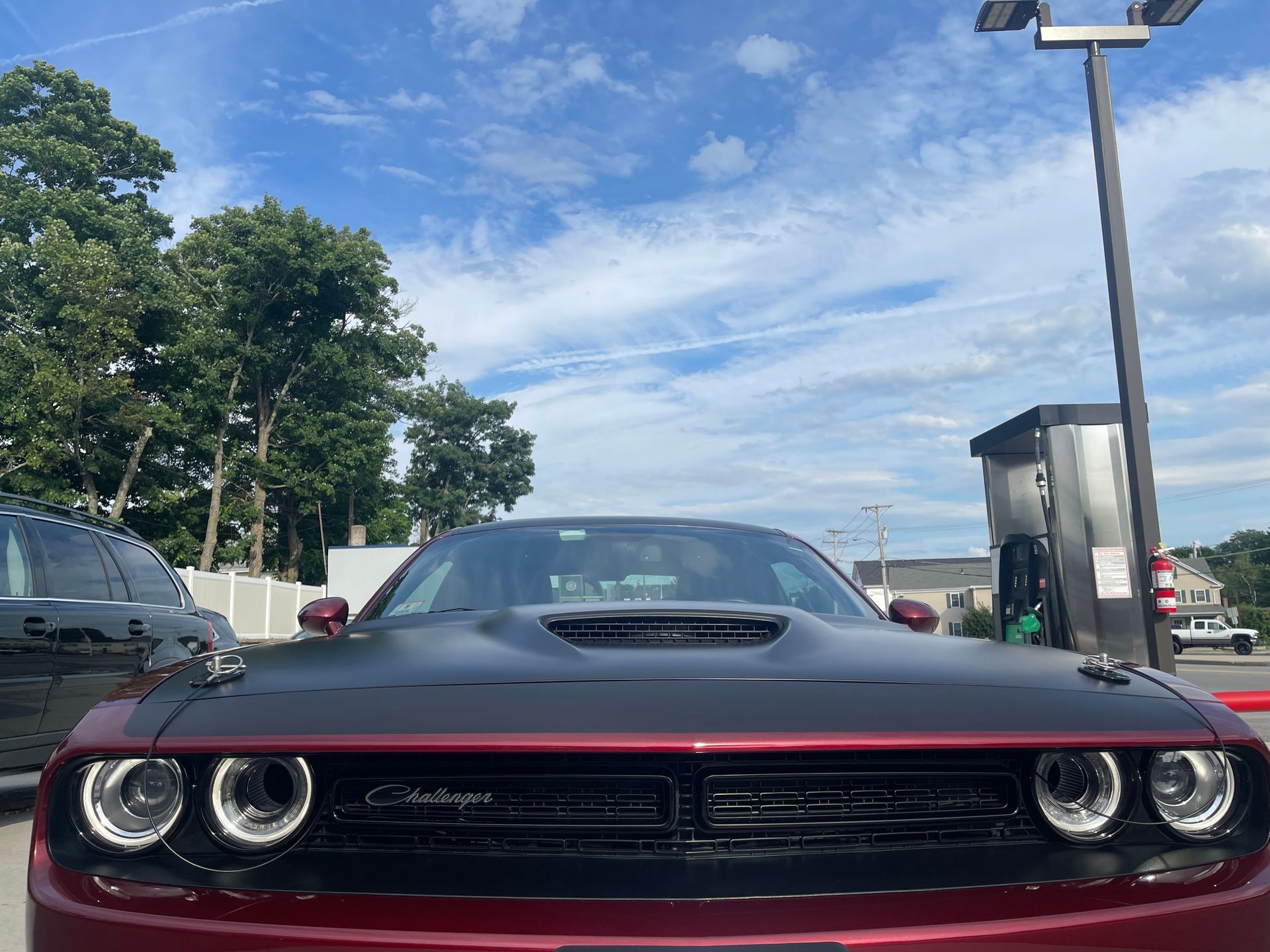 A red dodge challenger is parked in a parking lot next to a gas pump.