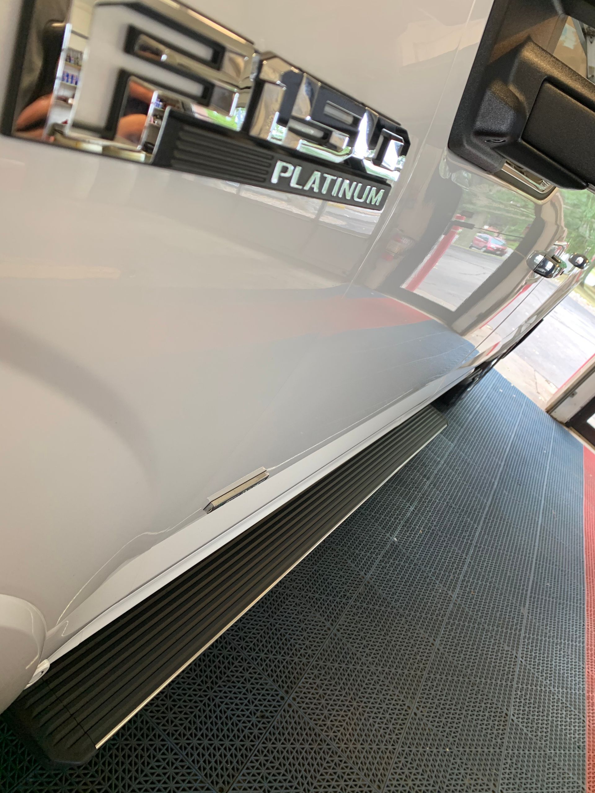 A white truck with black side steps is parked in a garage.