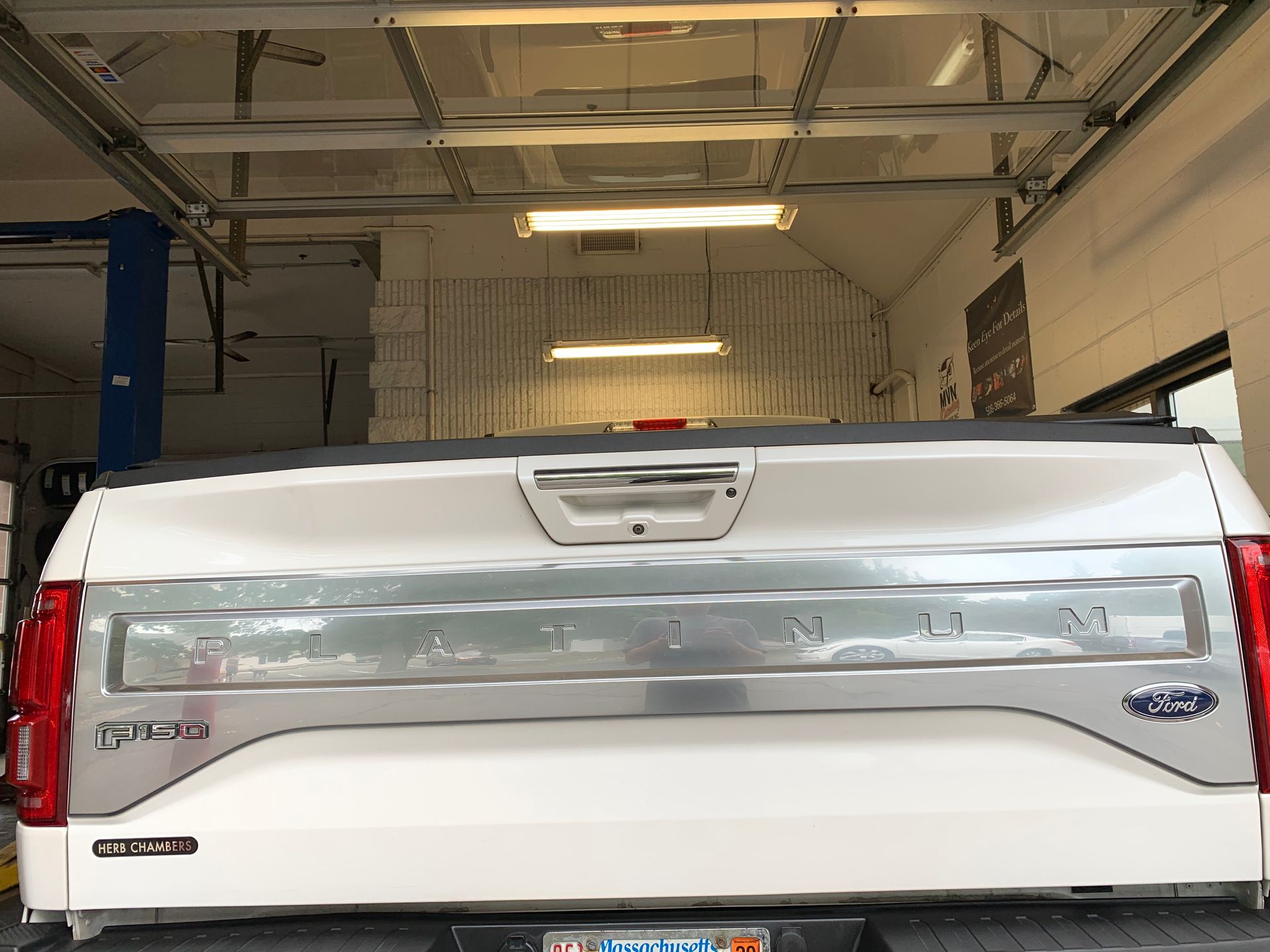 A white truck is parked in a garage with its tailgate open.