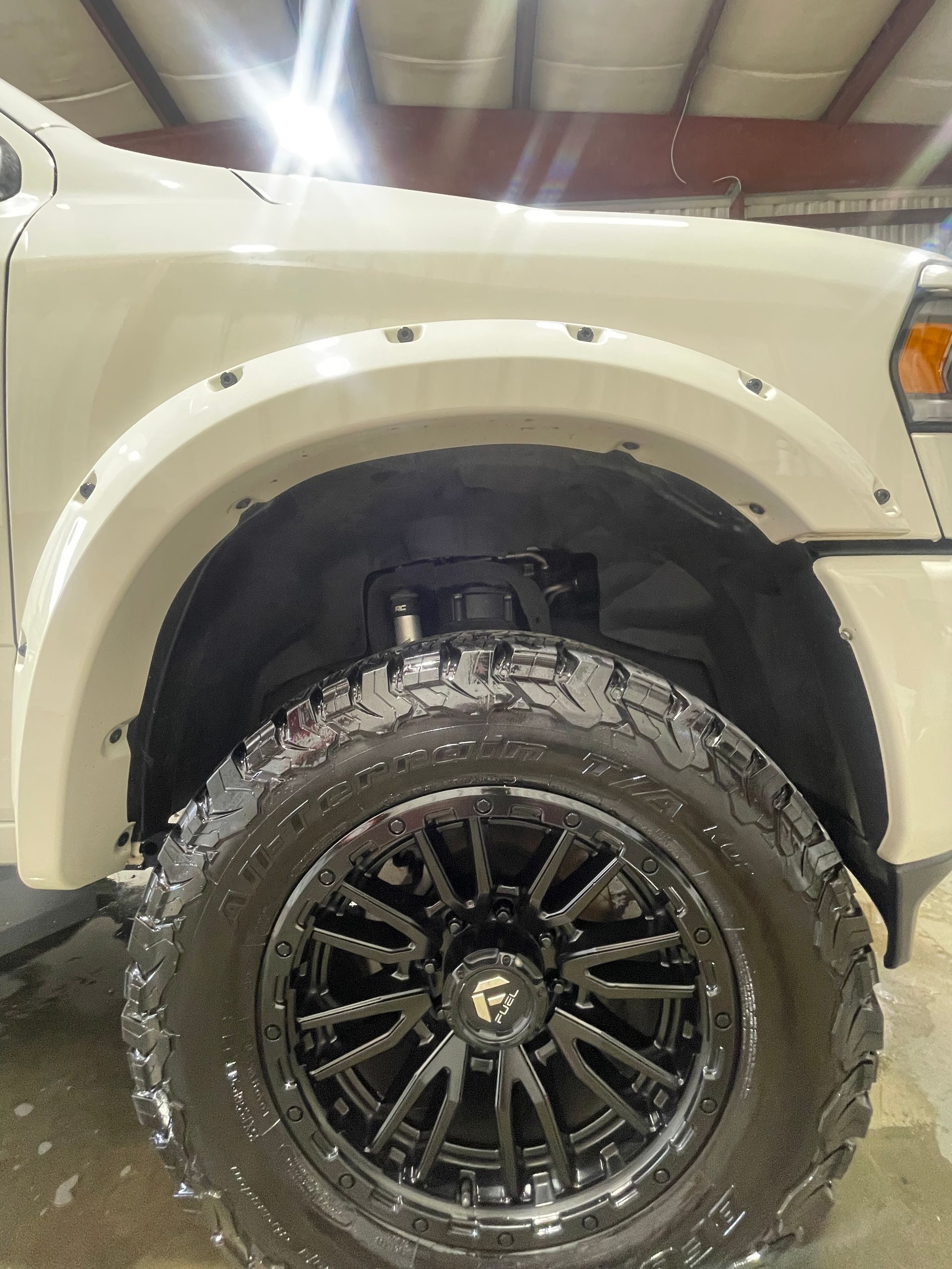 A white truck with black wheels and tires is parked in a garage.