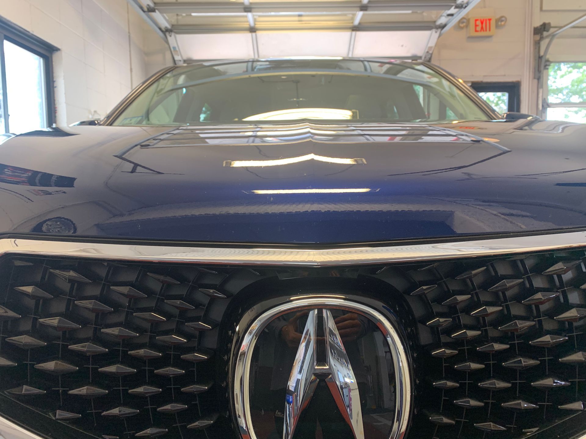 A blue acura is parked in a garage with the hood up.