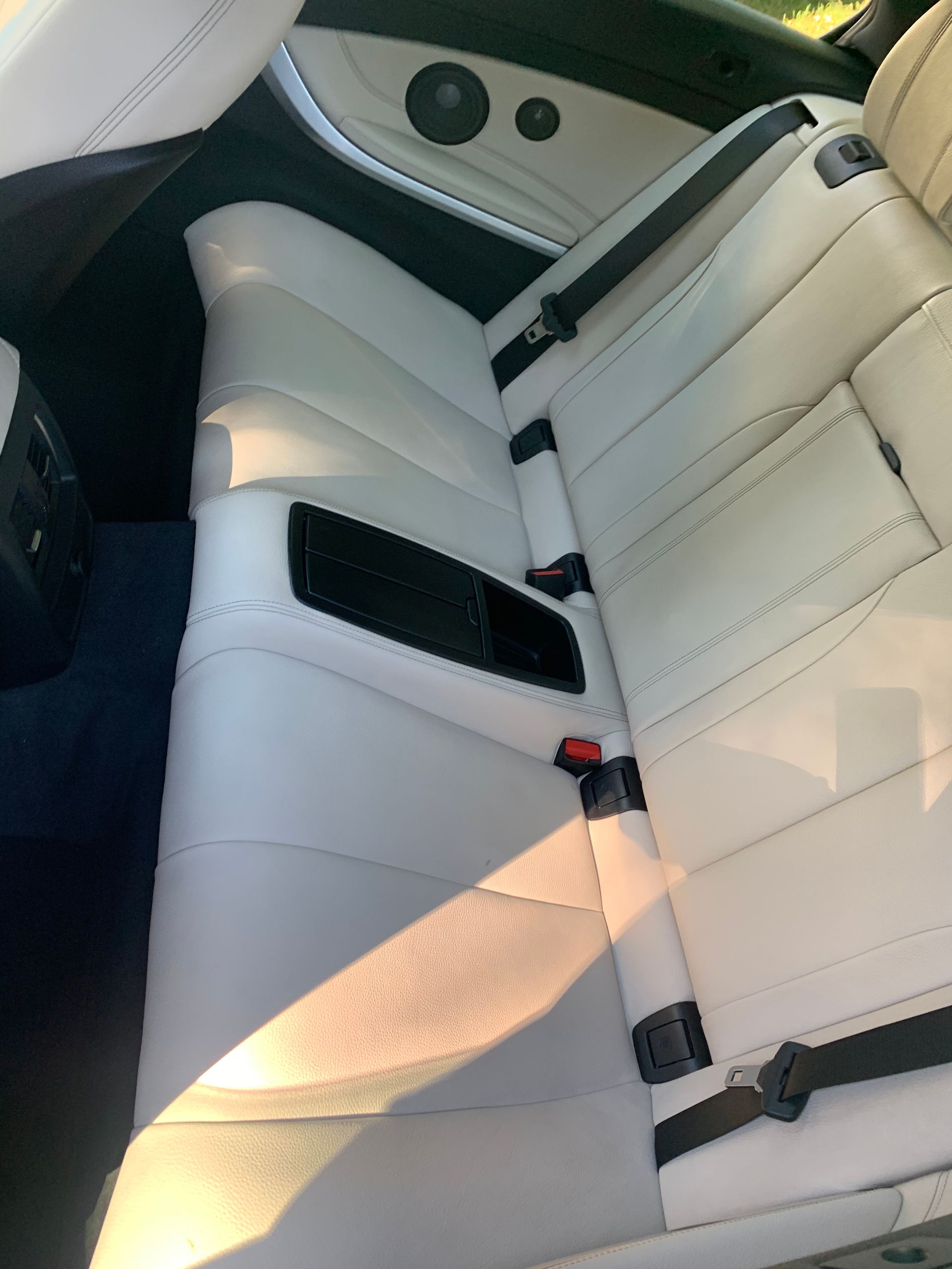 The back seat of a white car with black seat belts