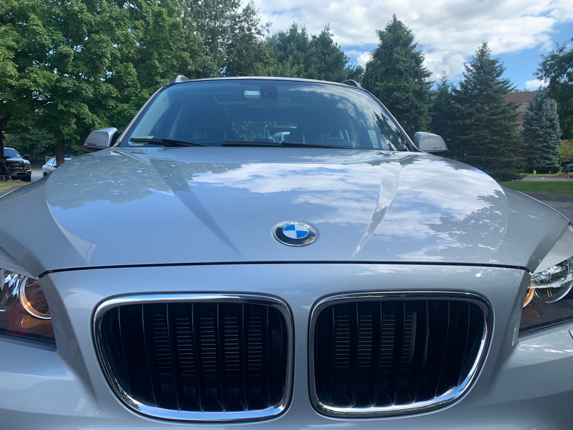 A silver bmw is parked in a driveway with trees in the background.
