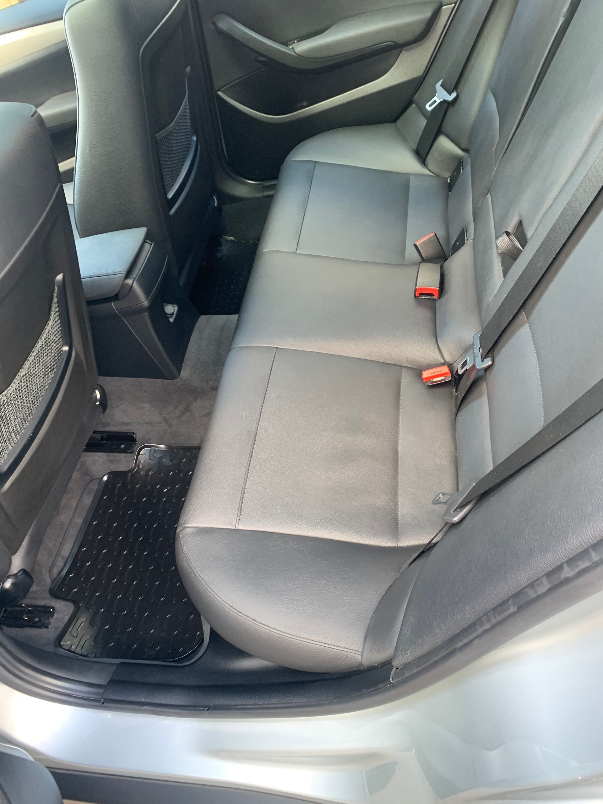The back seat of a silver car with black seat belts