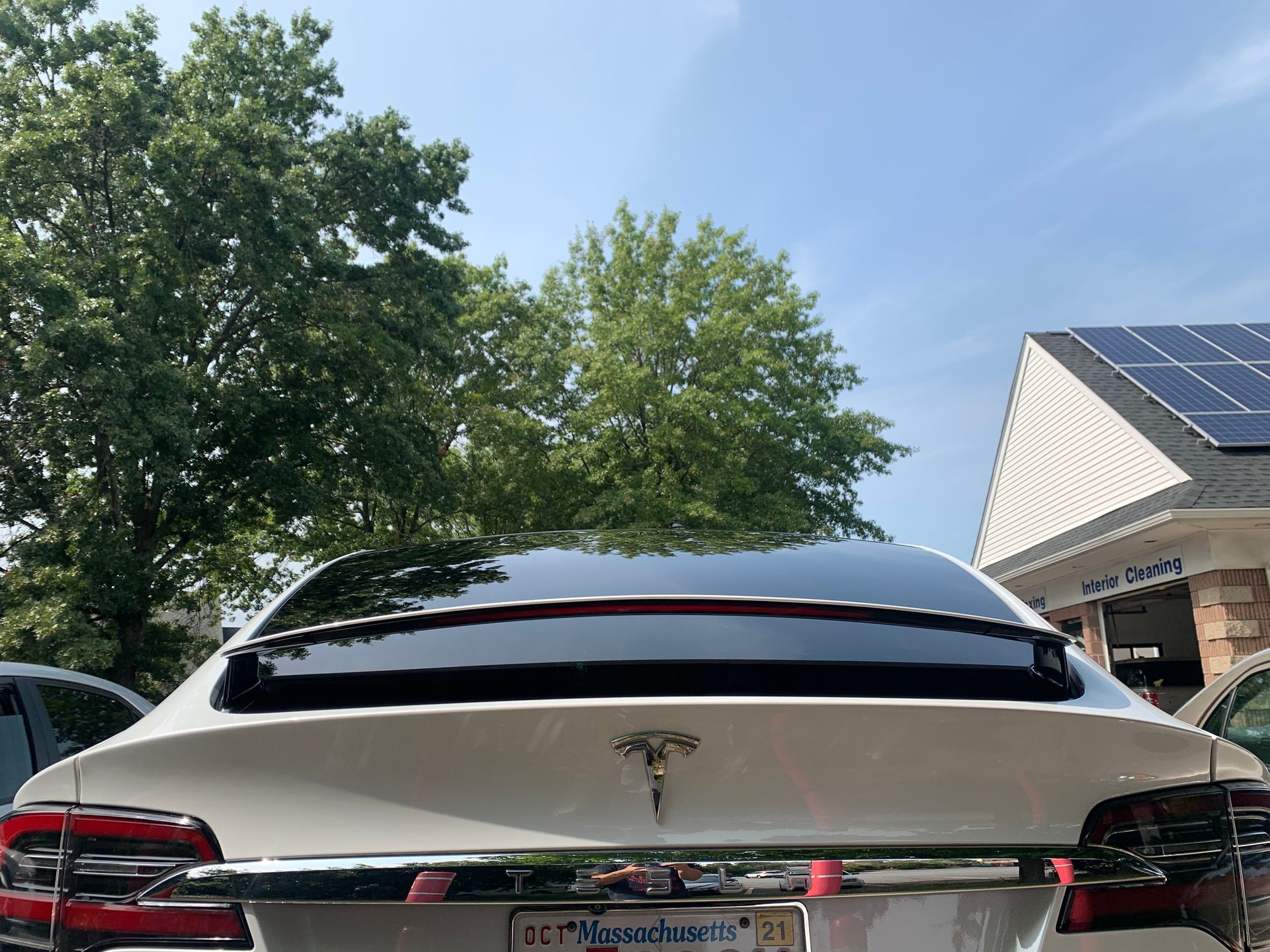 A white tesla model 3 is parked in front of a house with solar panels on the roof.