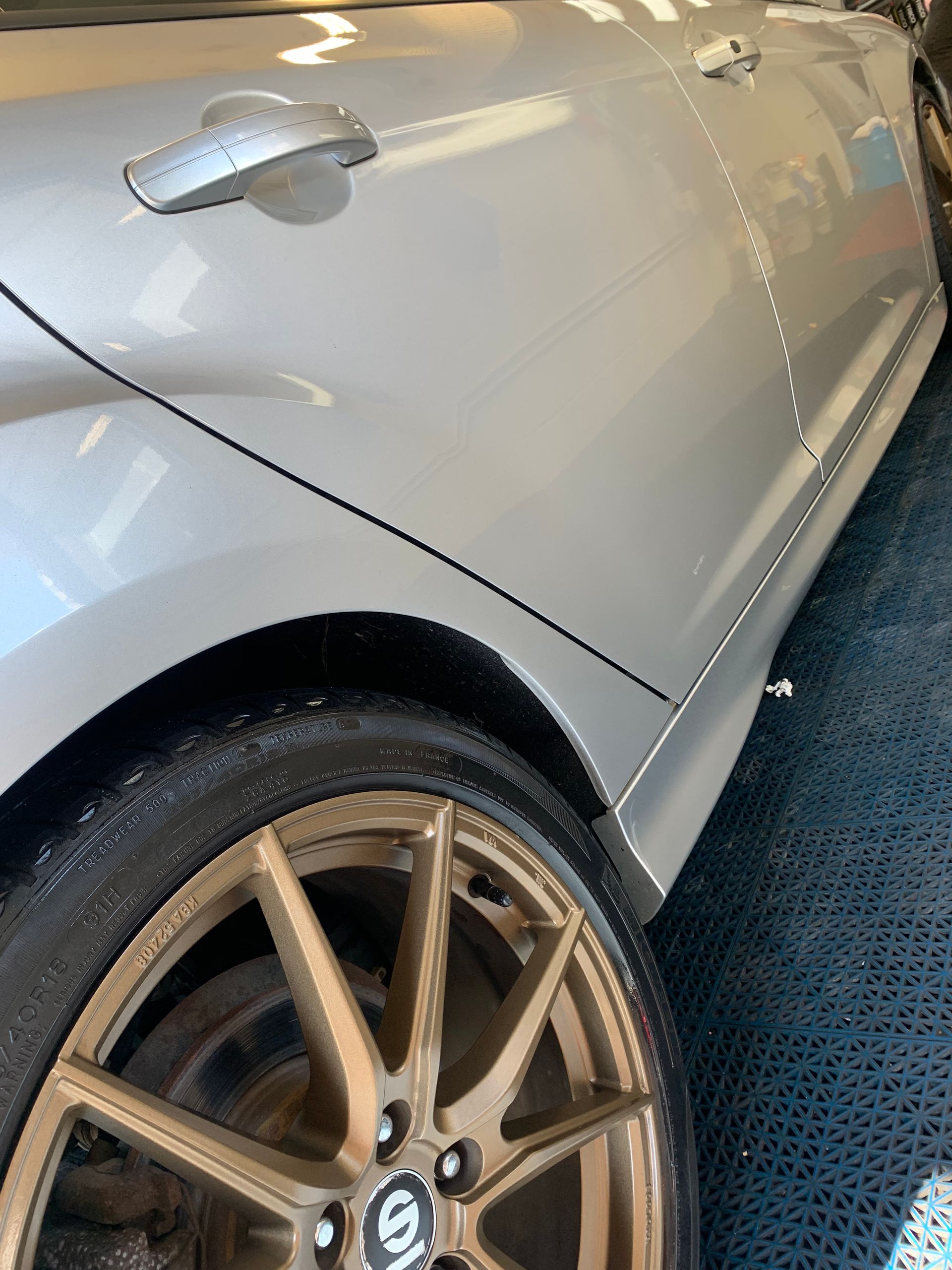 A silver car with gold wheels and tires is parked in a garage.