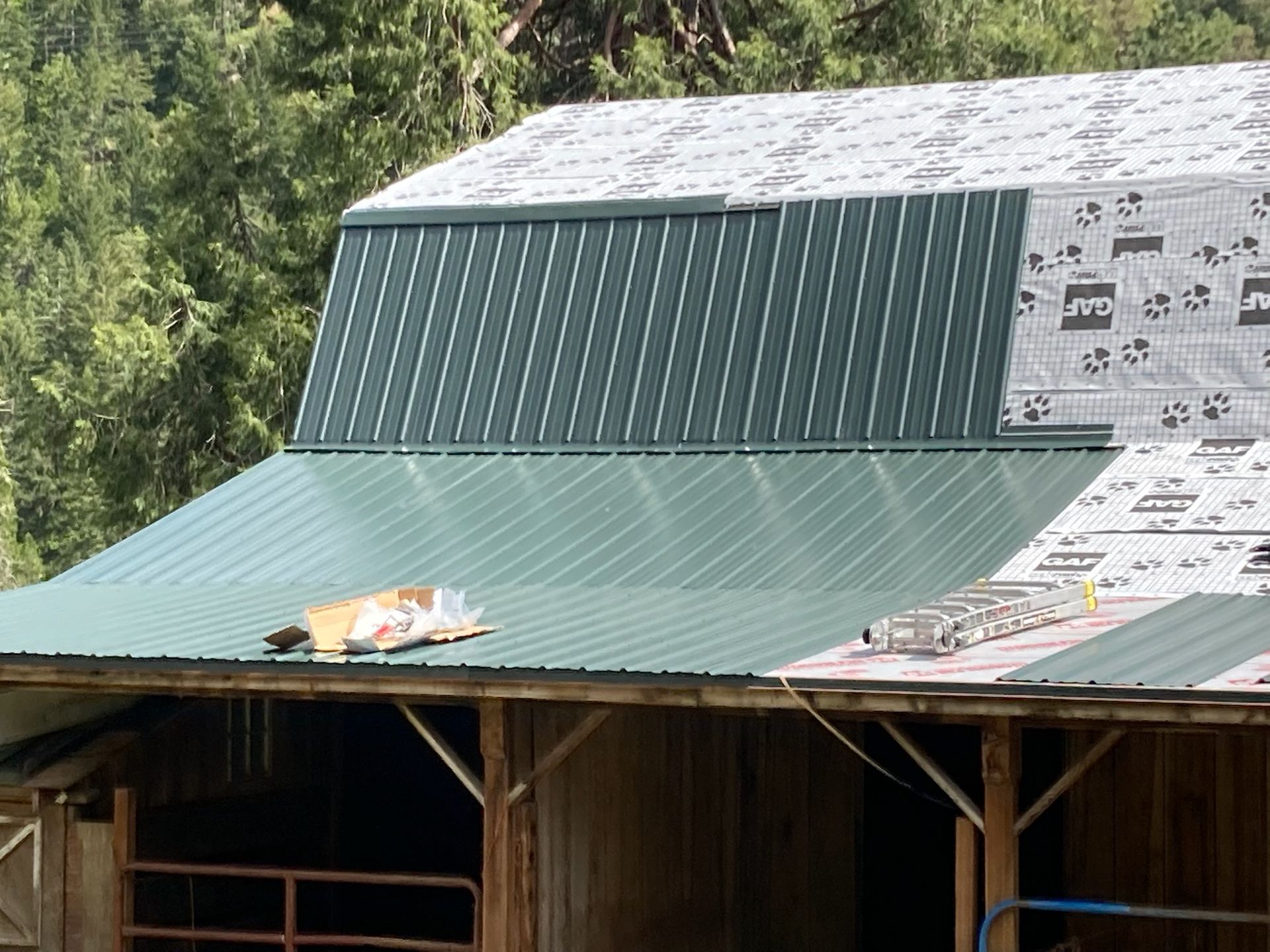 A green metal roof is being installed on a barn.