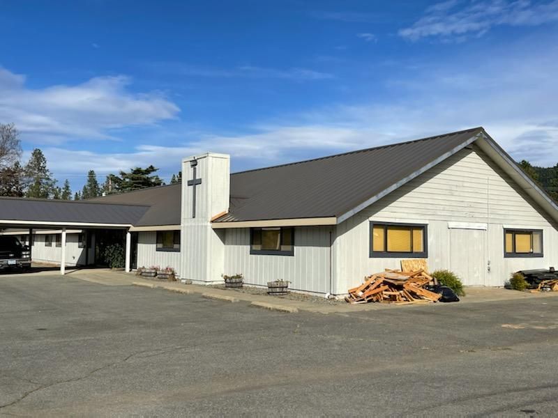 A small white house with a gray roof and a cross on the side.
