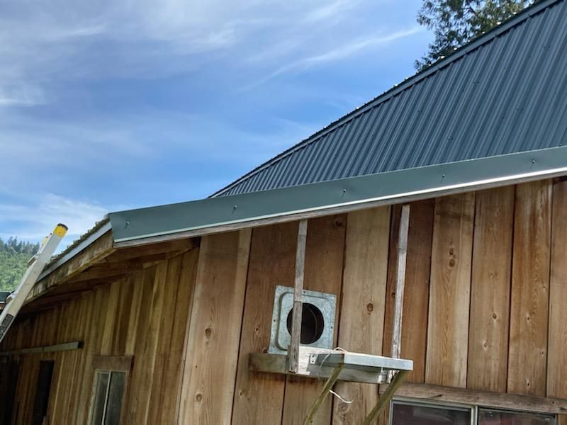 A wooden building with a metal roof and a fan on the side.