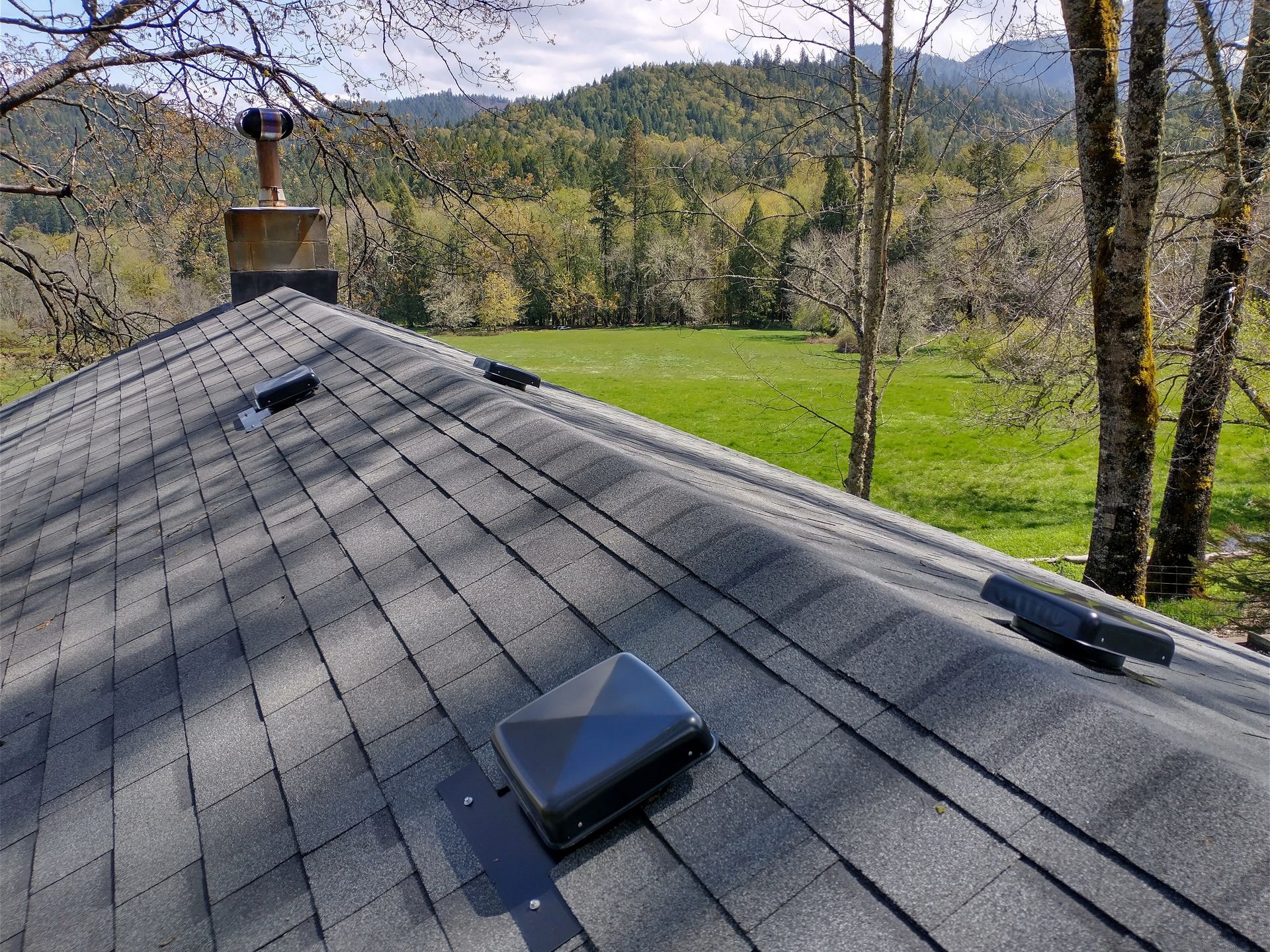 The roof of a house with a view of a field and mountains in the background.