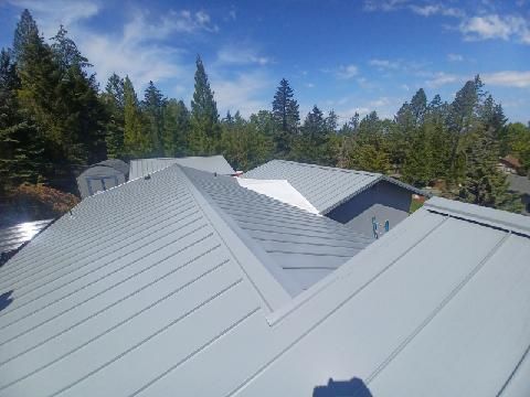 The roof of a house with a gray roof and trees in the background.