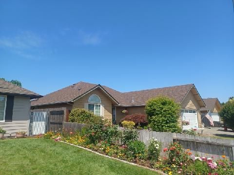 A house with a brown roof is surrounded by flowers and a fence.