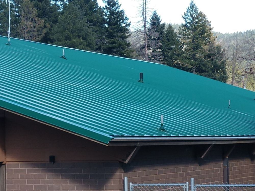 A brick building with a green roof and trees in the background