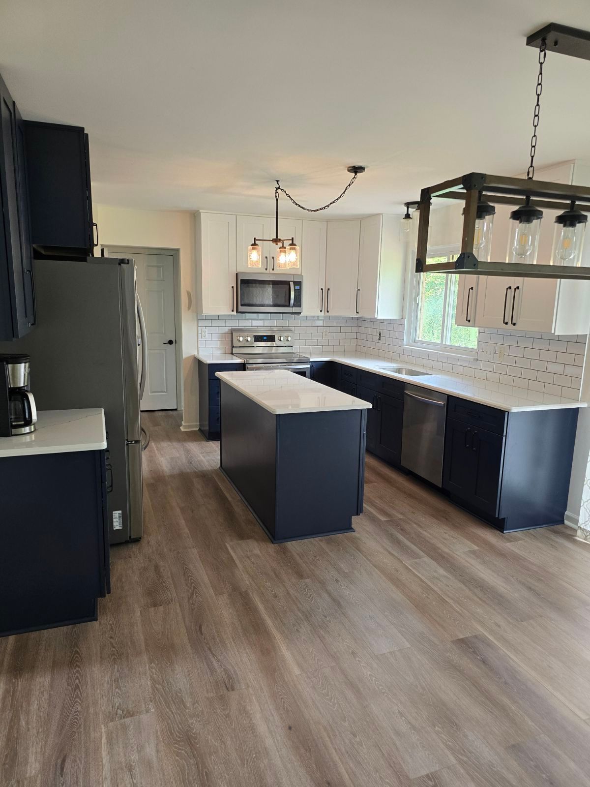 A kitchen with blue cabinets , white cabinets , stainless steel appliances and a large island.