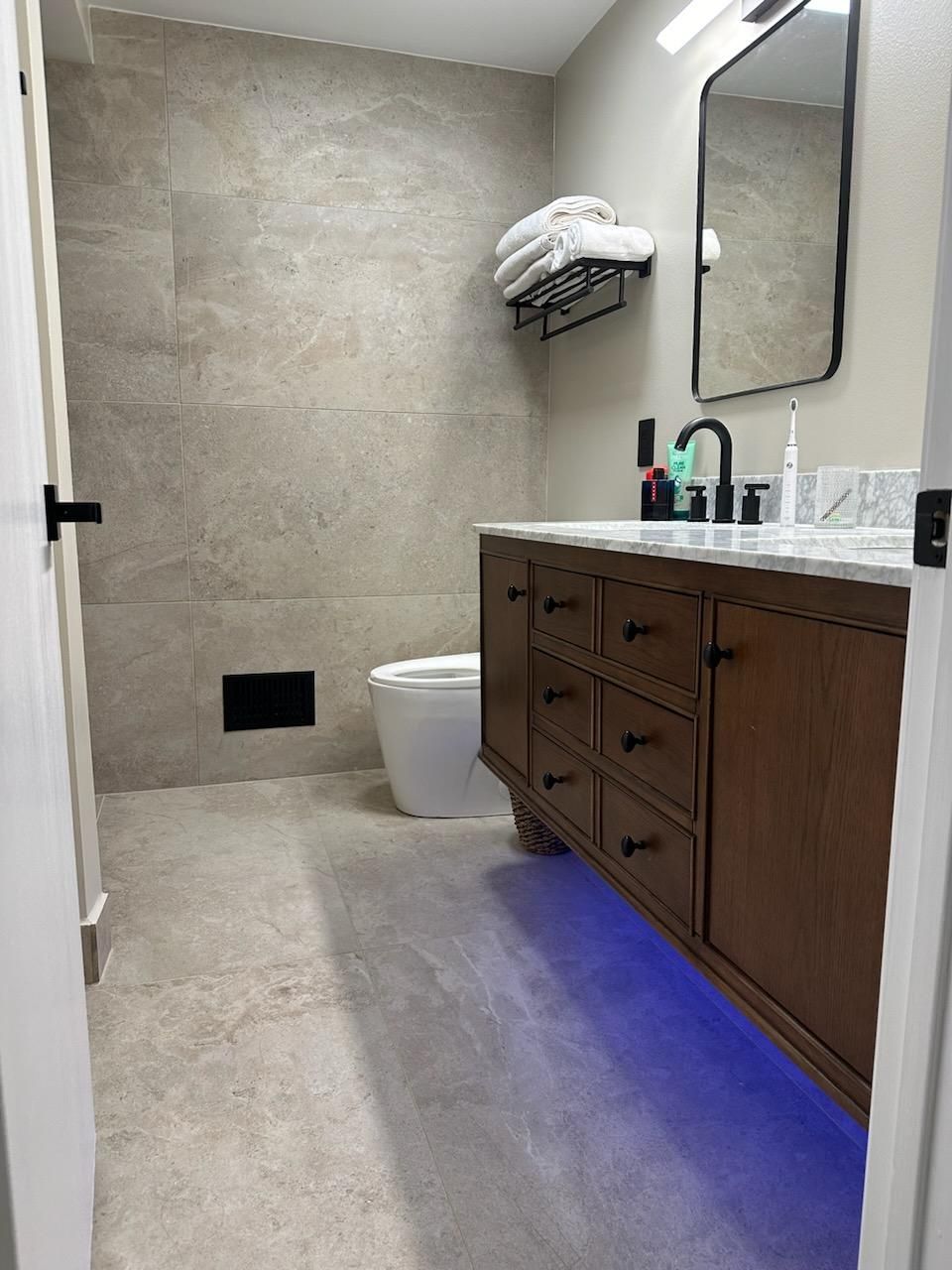 A  tile bathroom with a toilet , floating vanity and mirror.