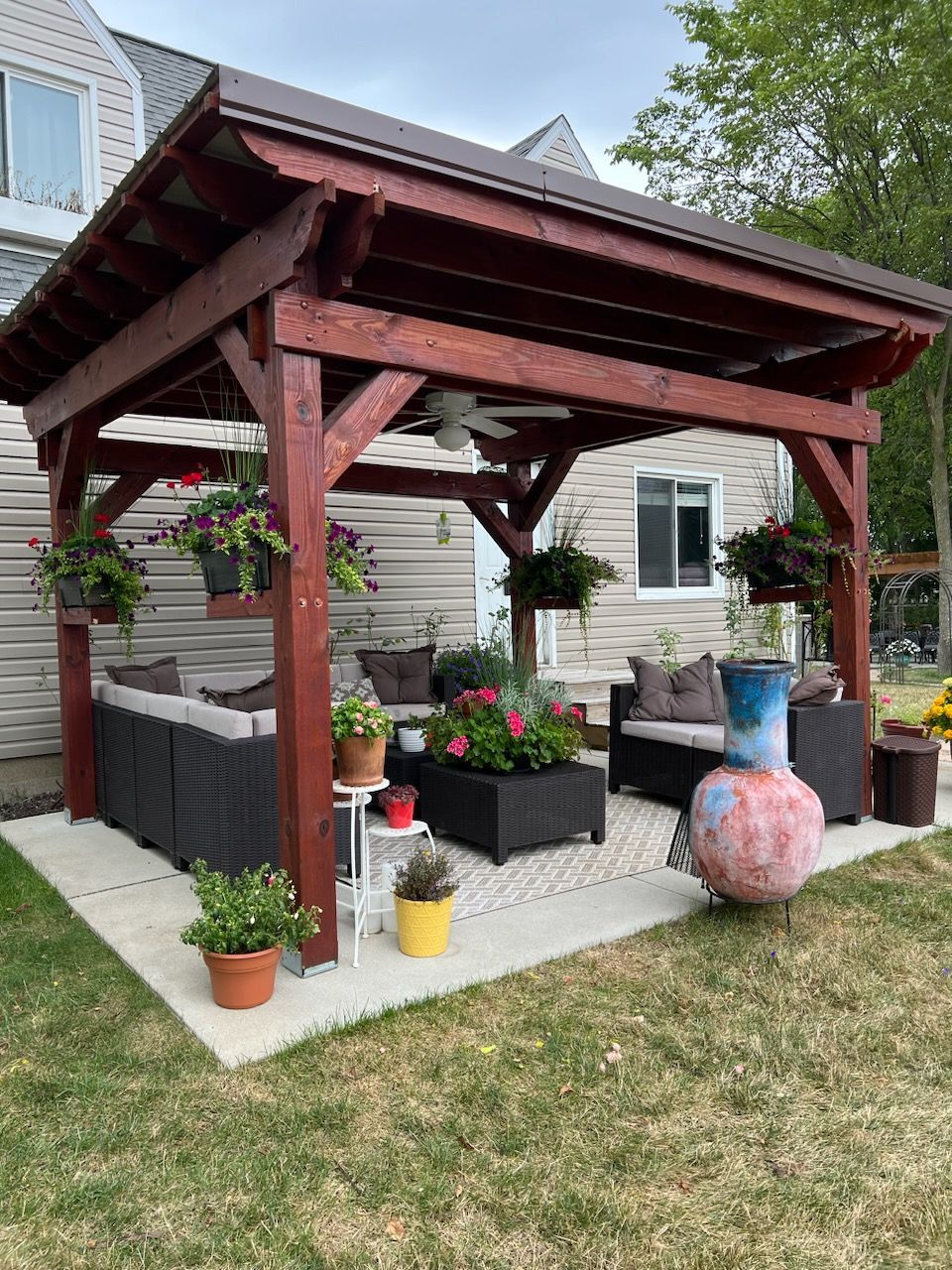 A wooden pergola with a couch and chairs underneath it in a backyard.
