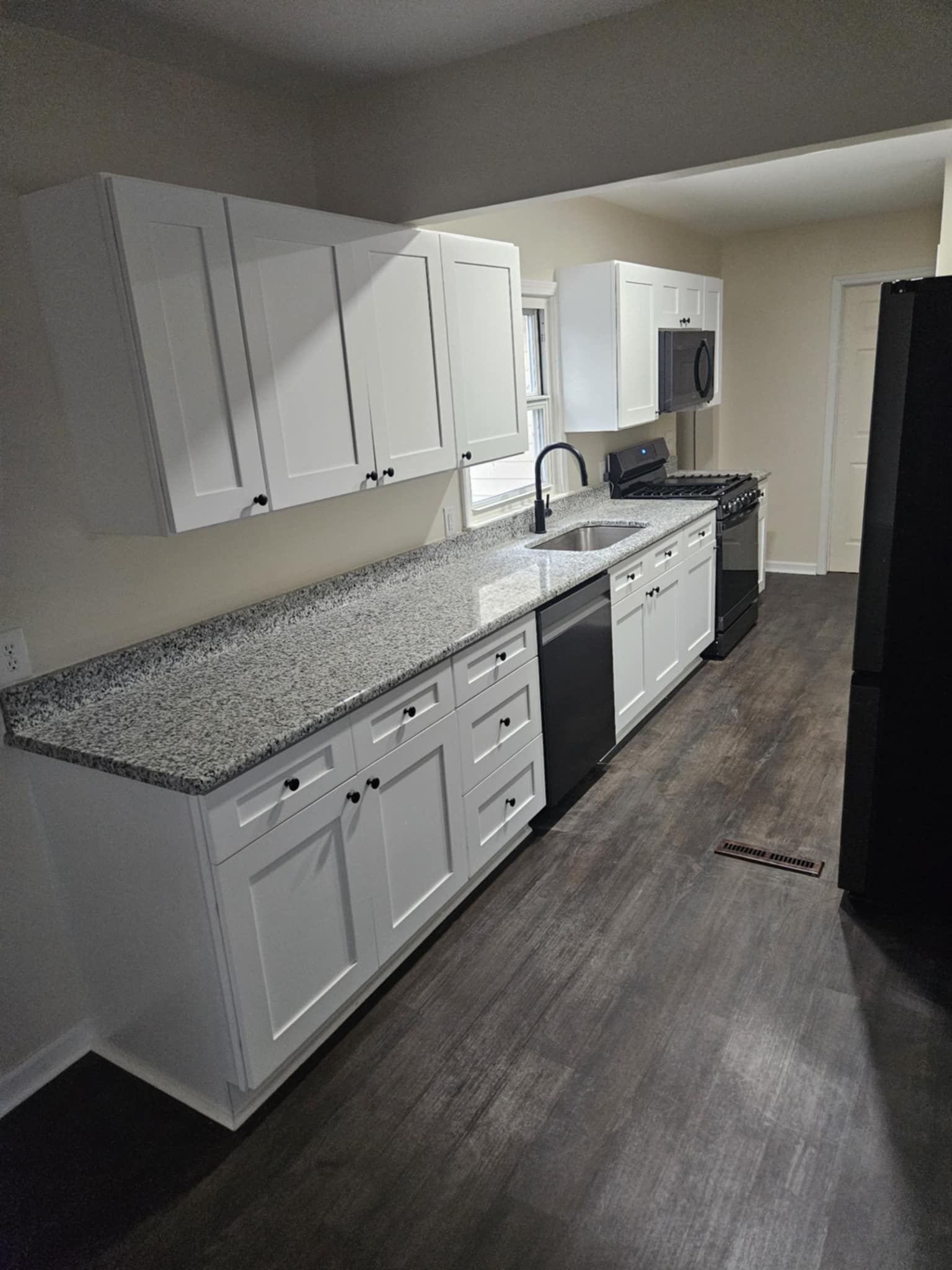 A kitchen with white cabinets , granite counter tops , black appliances and a black refrigerator.