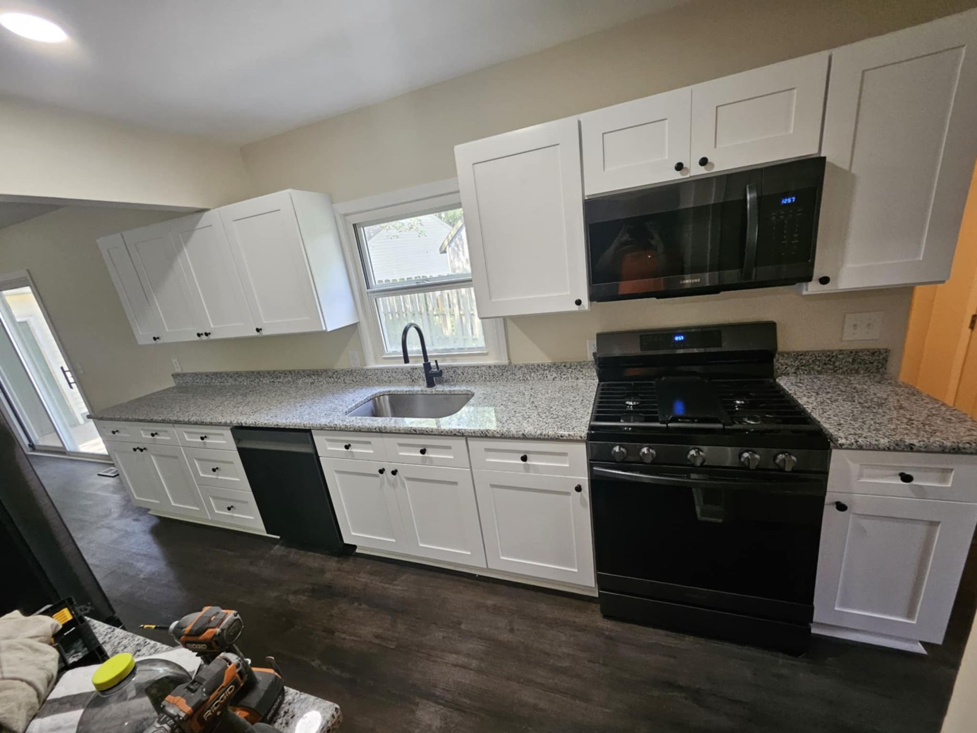 A kitchen with white cabinets , black appliances , granite counter tops , and a sink.
