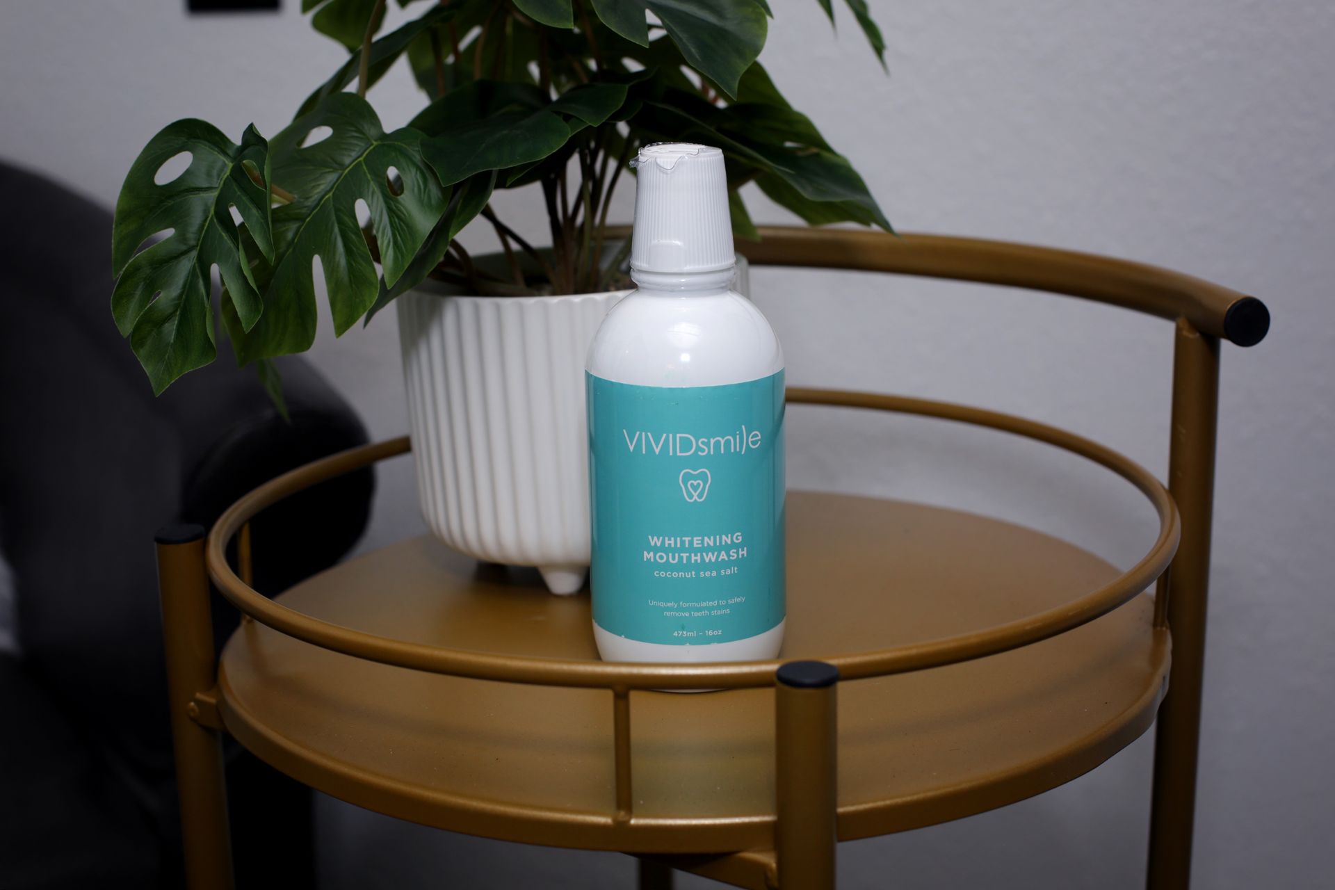 White bottle of mouthwash on a gold table next to a potted plant, set against a wall.