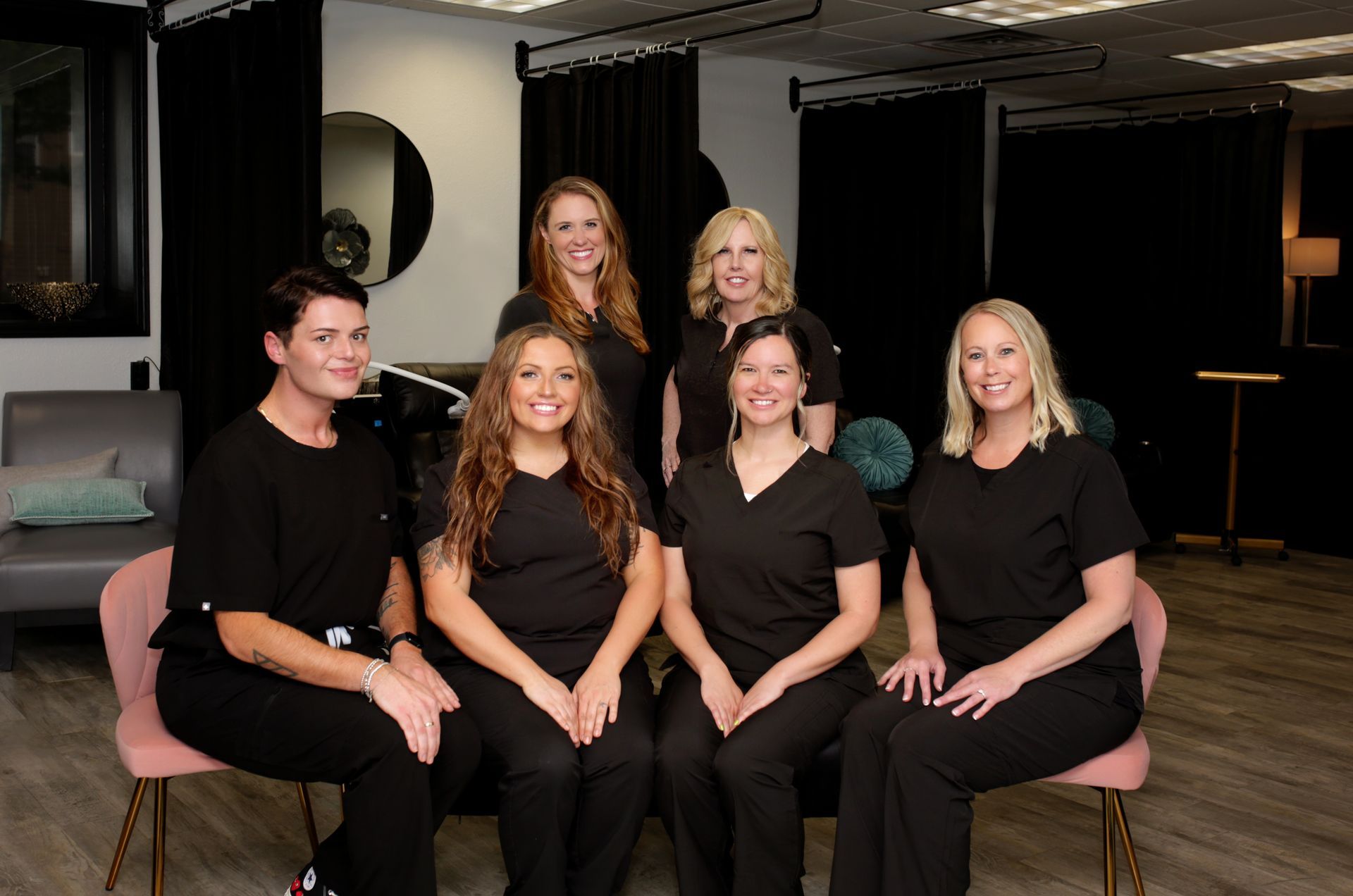 Group of seven people in black scrubs, posed in a modern office setting.