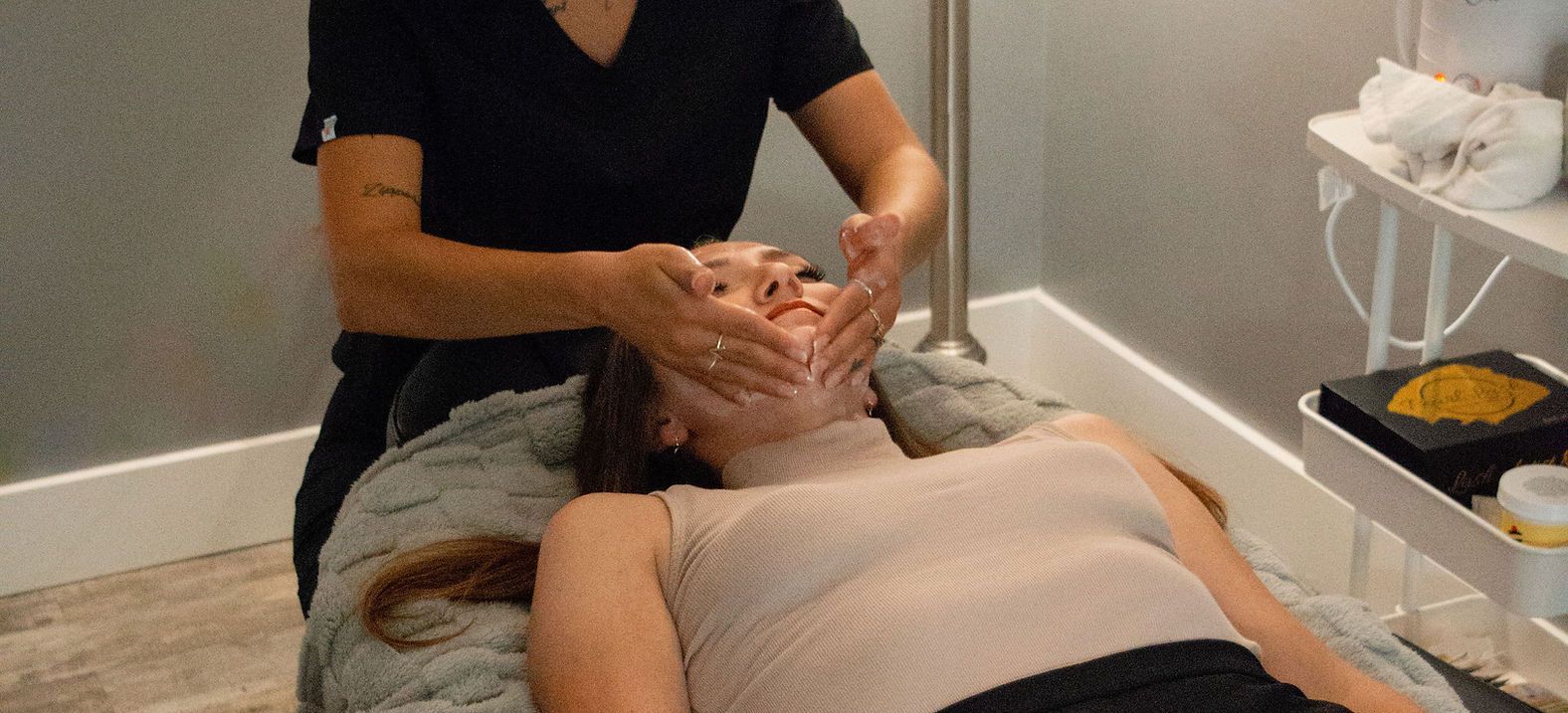 Woman receiving facial massage from another woman in a spa-like setting.