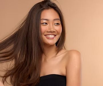 Smiling Asian woman with long brown hair and a black strapless top, tan background.