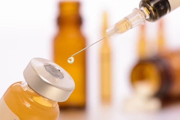 Syringe drawing liquid from a vial; amber glass bottles in the background.