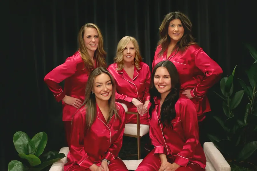 Five women in red silk pajamas pose in a studio setting.