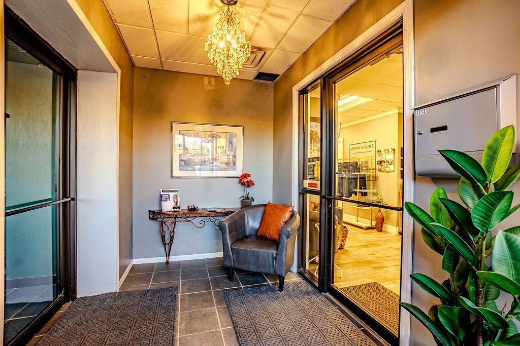 Hallway with a dark gray armchair, console table, and glass doors; neutral tones.