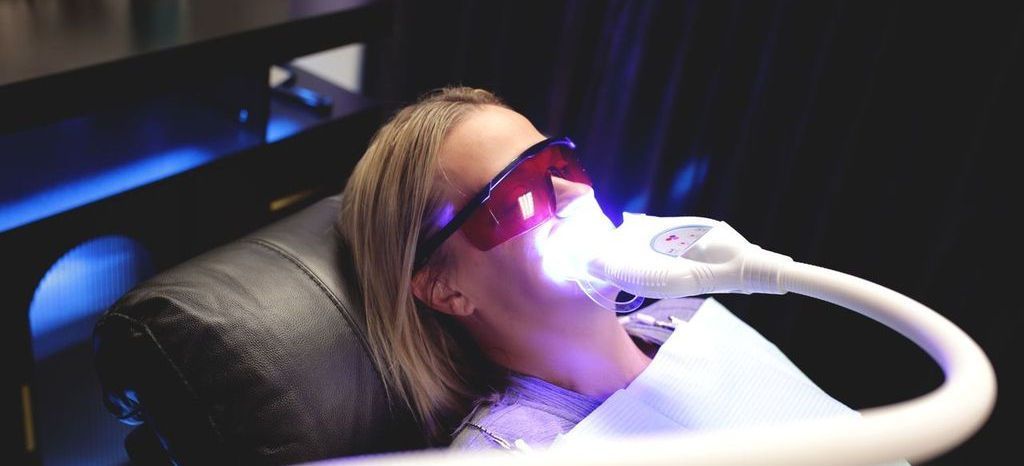 Woman in a dental chair with a bright light shining on her teeth, wearing protective glasses.