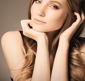 Woman with long wavy hair, resting her chin on her hands, looking thoughtful.