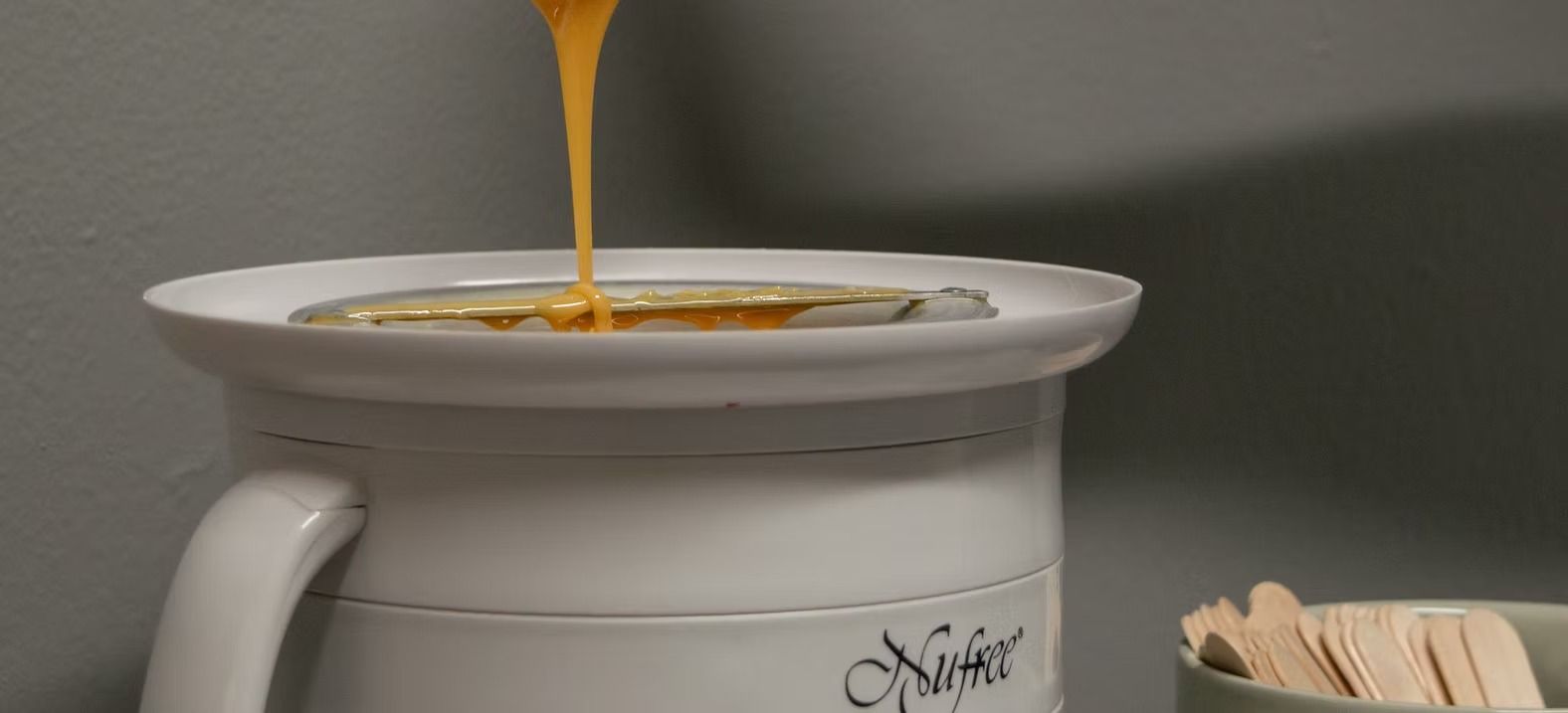 Wax being poured into a white warmer. Wooden applicators in a container on the right.