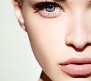Close-up of a fair-skinned woman with blue eyes and pink lips, bathed in soft light.