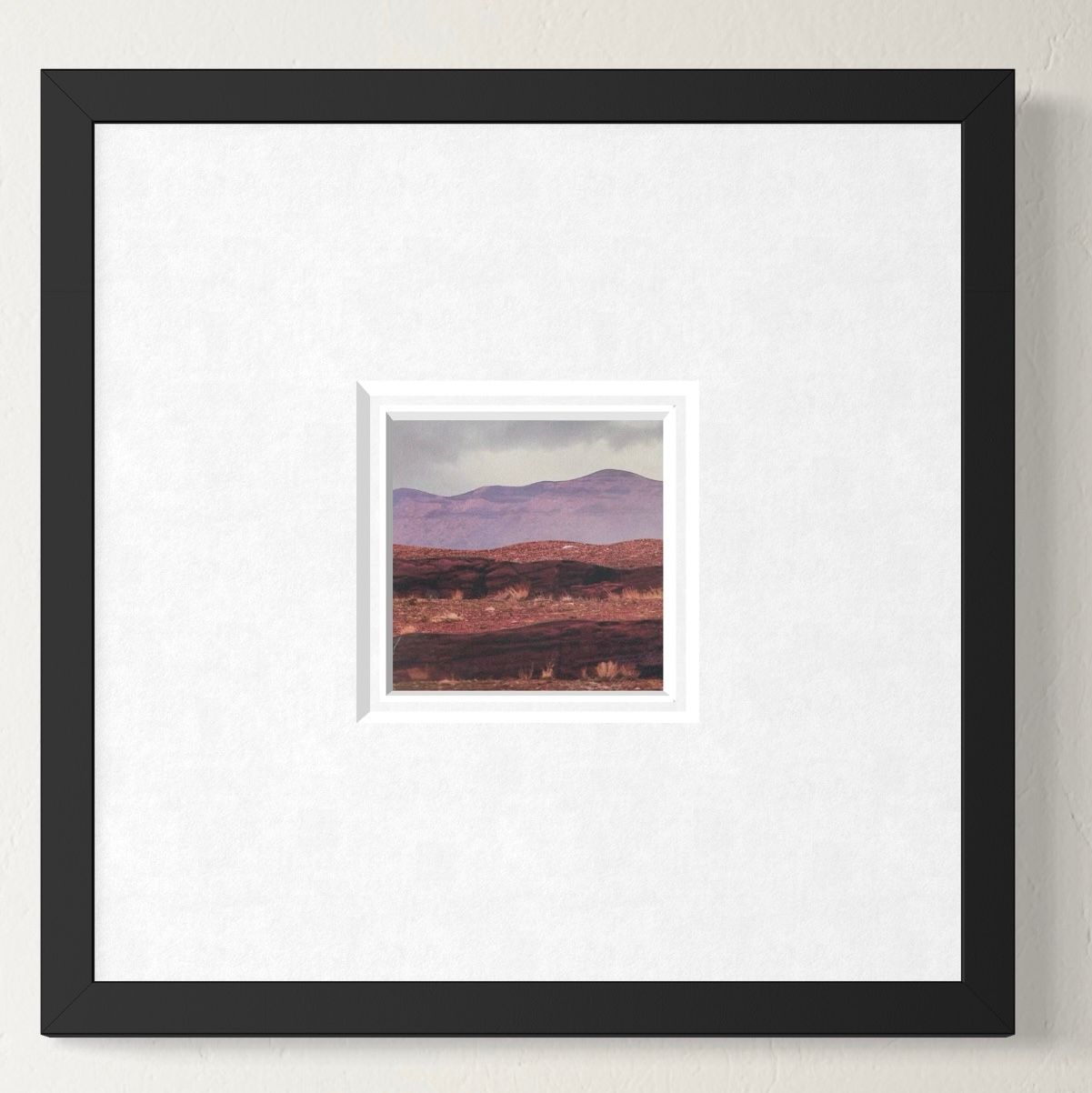 Reddish-brown hills and mountains under a cloudy, gray sky. Some dried grass in foreground.