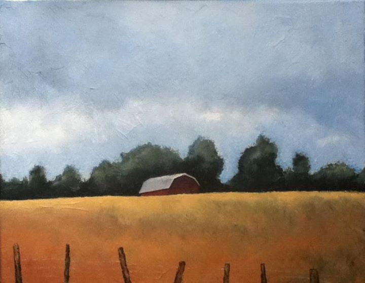 Red barn in a field of gold, with trees against a cloudy sky.