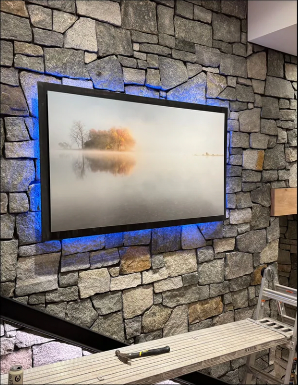 A flat screen tv is mounted on a stone wall.