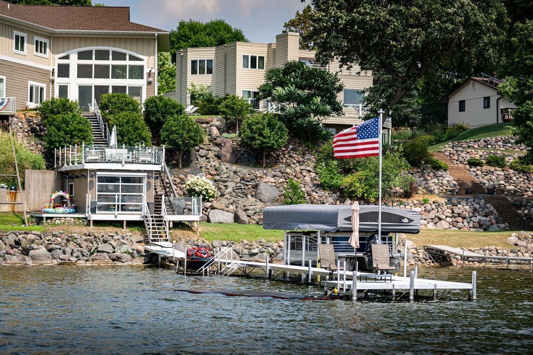 A large house sits on the shore of a lake with a boat docked in front of it.