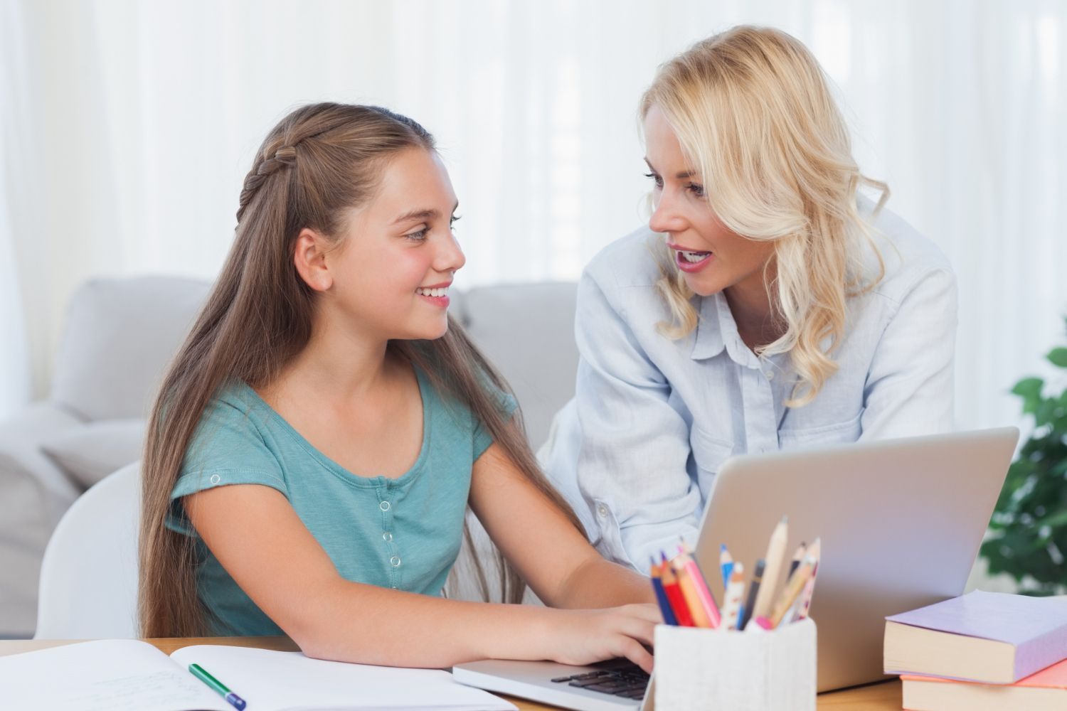 A woman and a girl are sitting at a table looking at a laptop computer.