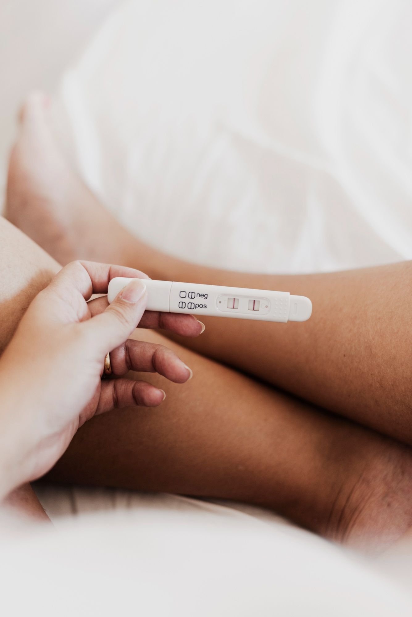 A woman is laying on a bed holding a pregnancy test.