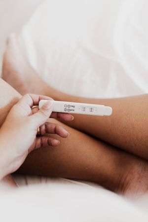 A woman is laying on a bed holding a pregnancy test.