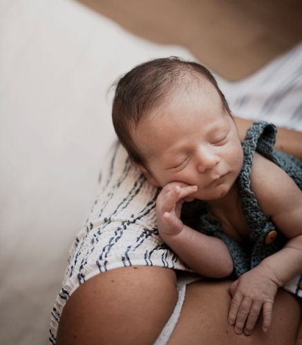 A newborn baby is sleeping on a woman 's shoulder.