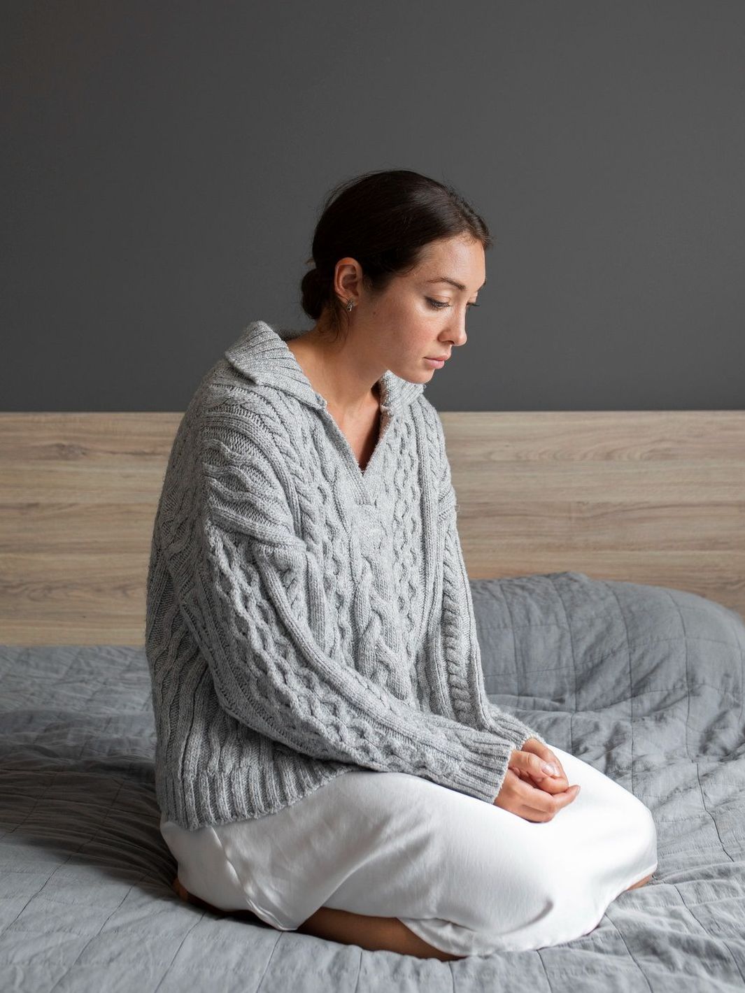 A woman in a sweater is sitting on a bed.