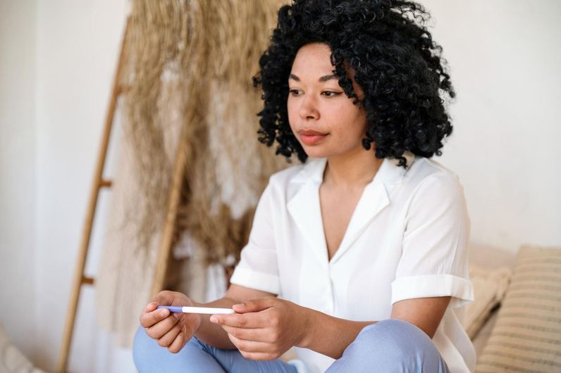 A woman is sitting on a couch holding a pregnancy test.