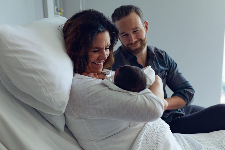 A man and a woman are holding a newborn baby in a hospital bed.