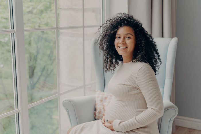 A pregnant woman is sitting in a chair in front of a window.