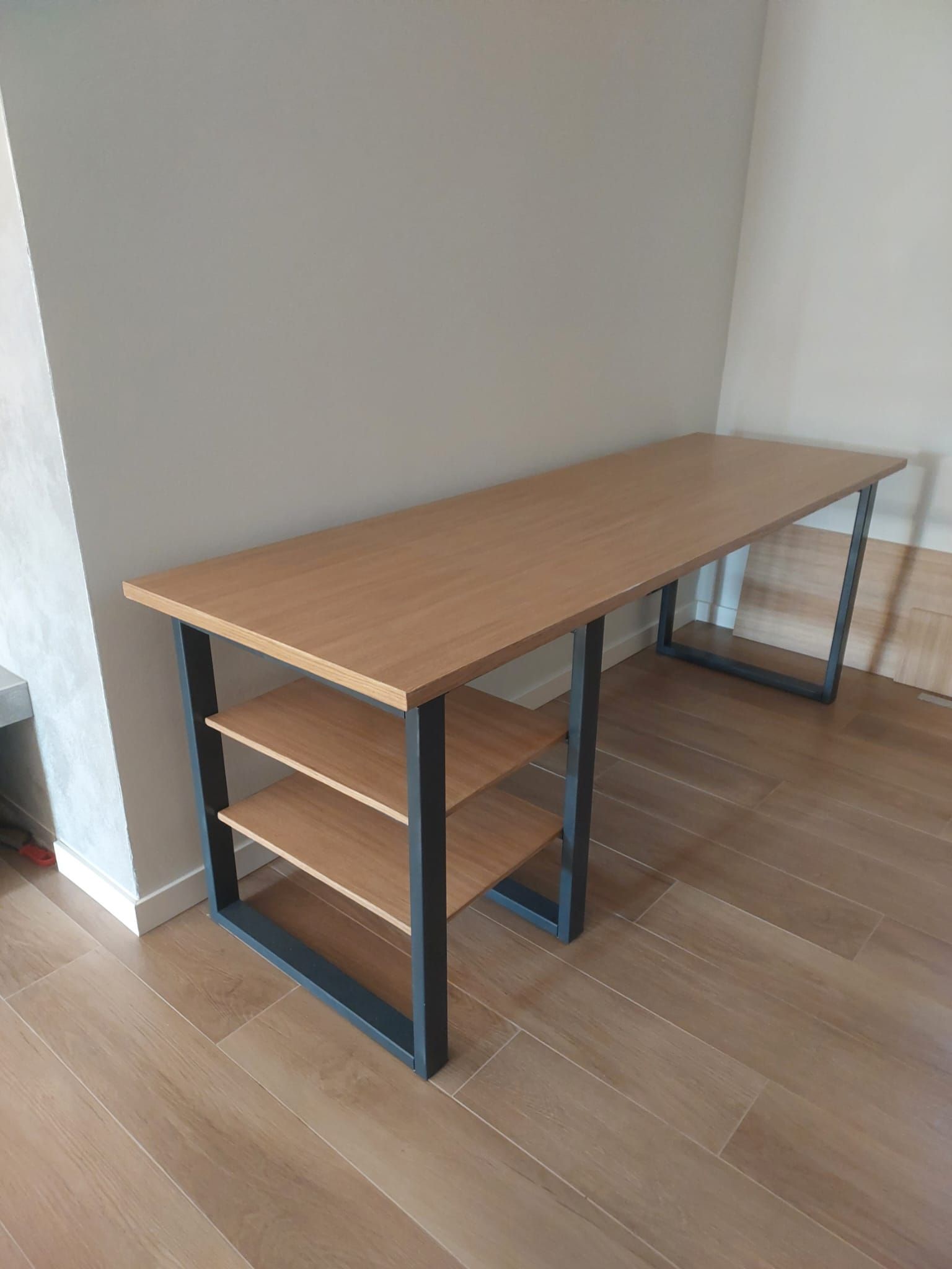 Una scrivania di legno con degli scaffali sottostanti in una stanza.