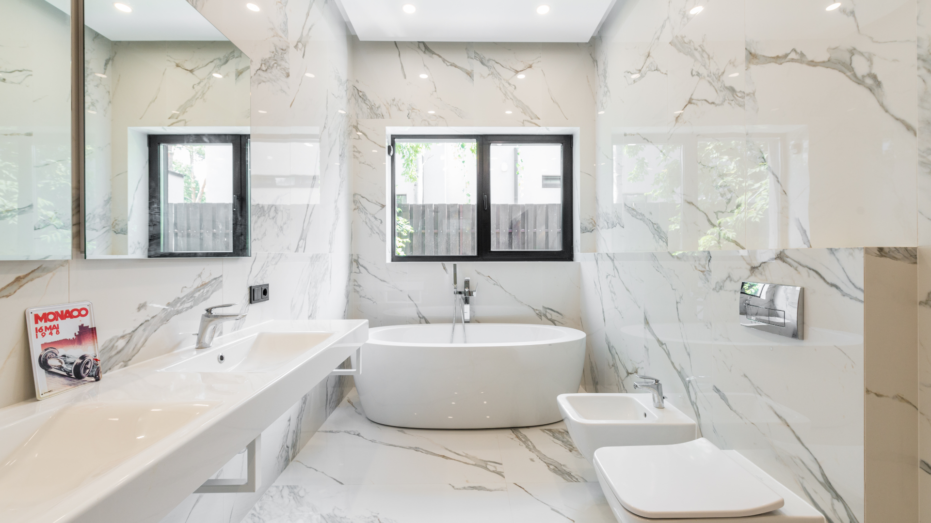 A modern, marble-tiled bathroom with a bathtub, sink, toilet, and window. The space is bright and minimalist.