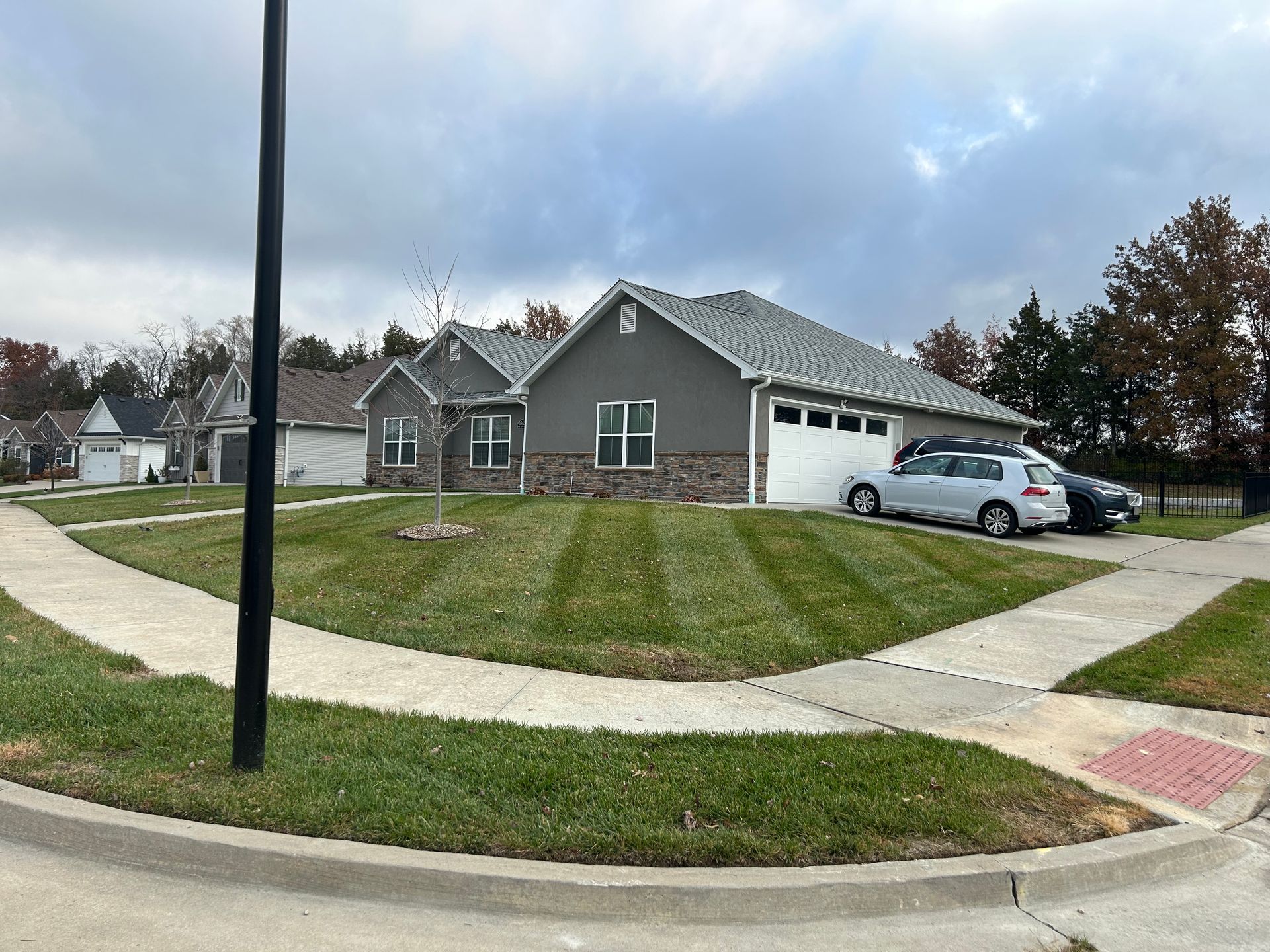 Suburban house with well-manicured lawn and parked cars on a cloudy day.