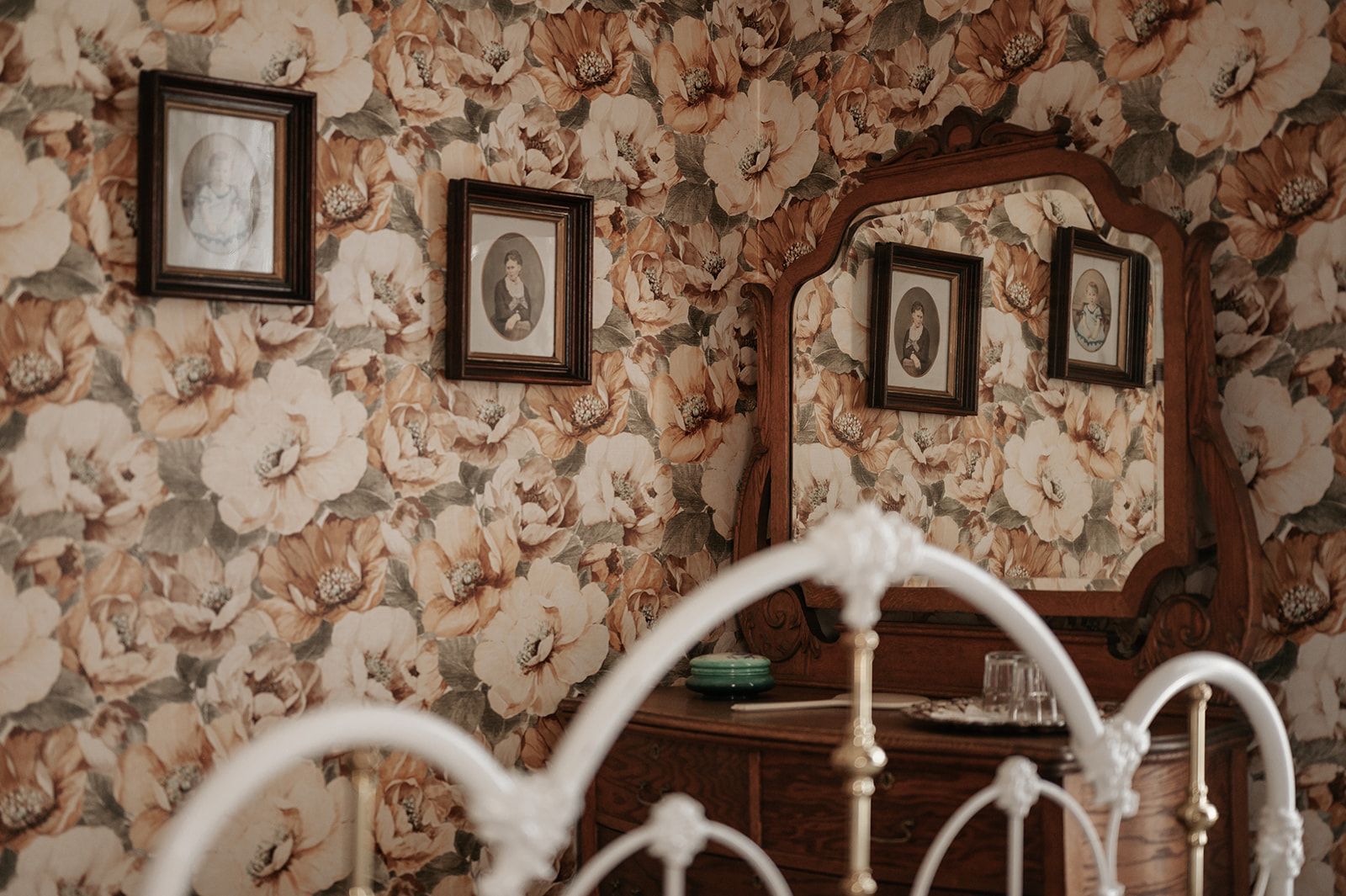 A bedroom with a bed , dresser , mirror and floral wallpaper.